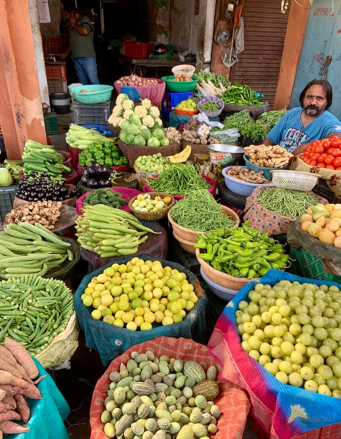 A vendor sitting behind baskets of beans, chillies, lemons and other vegetables